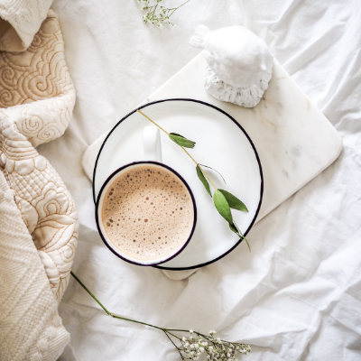 Latte on a plate with a green twig, blanket and florals