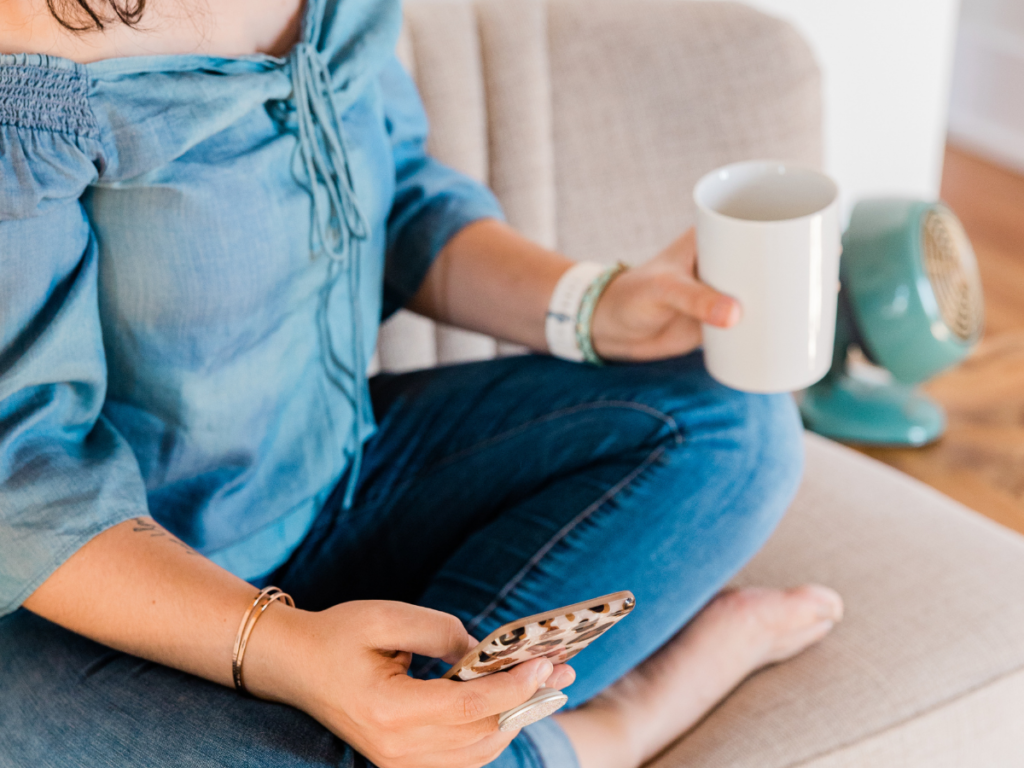 Sitting down in a blue shirt, holding a mug with my phone in the other hand