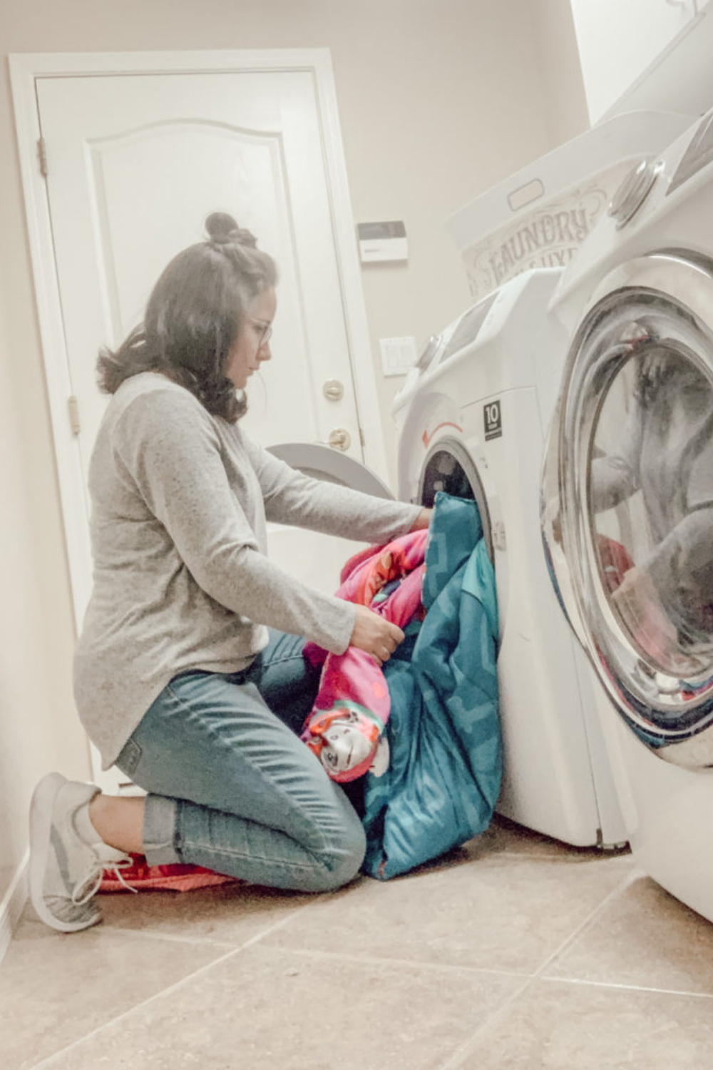 A woman kneeling down to put blankets into a washing machine