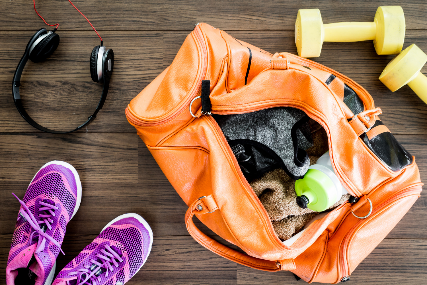 An orange gym bag surrounded by shoes, headphones, and weights