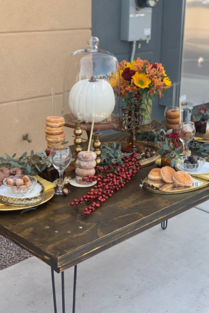 Table covered in donuts, fall decor items, and a white pumpkin