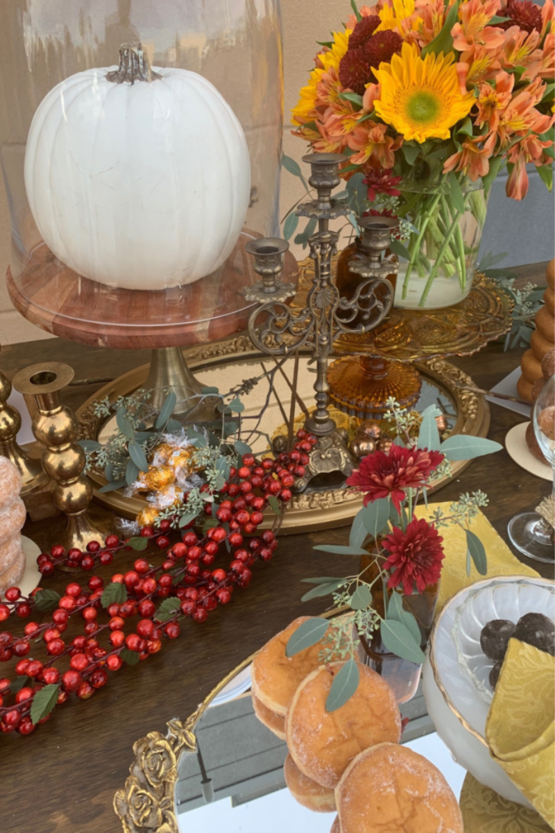 Table covered in donuts, fall decor items, and a white pumpkin