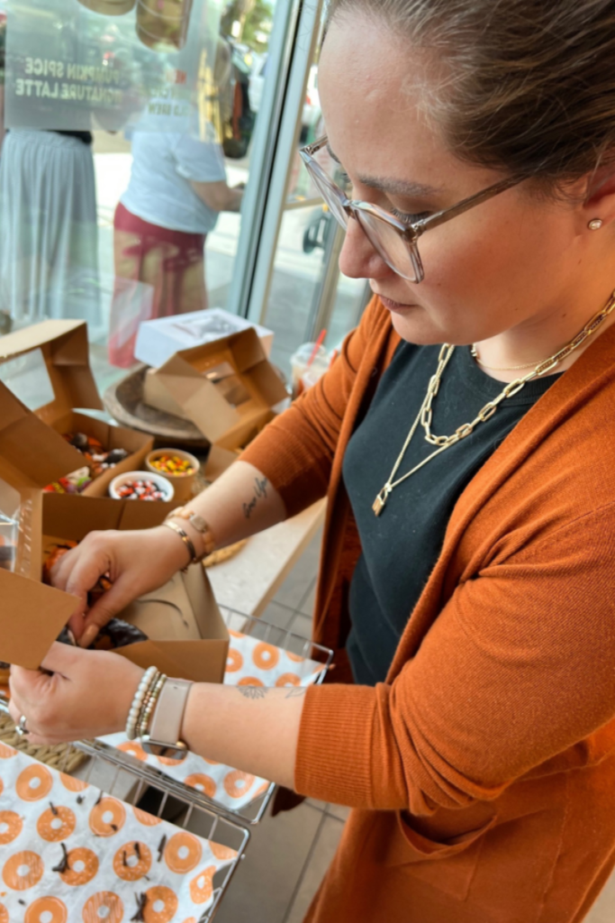 Putting together a box of donuts, wearing an orange sweater