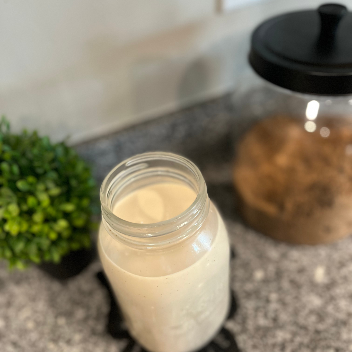 Cream in a glass mason jar with a green plant and jar of brown sugar behind