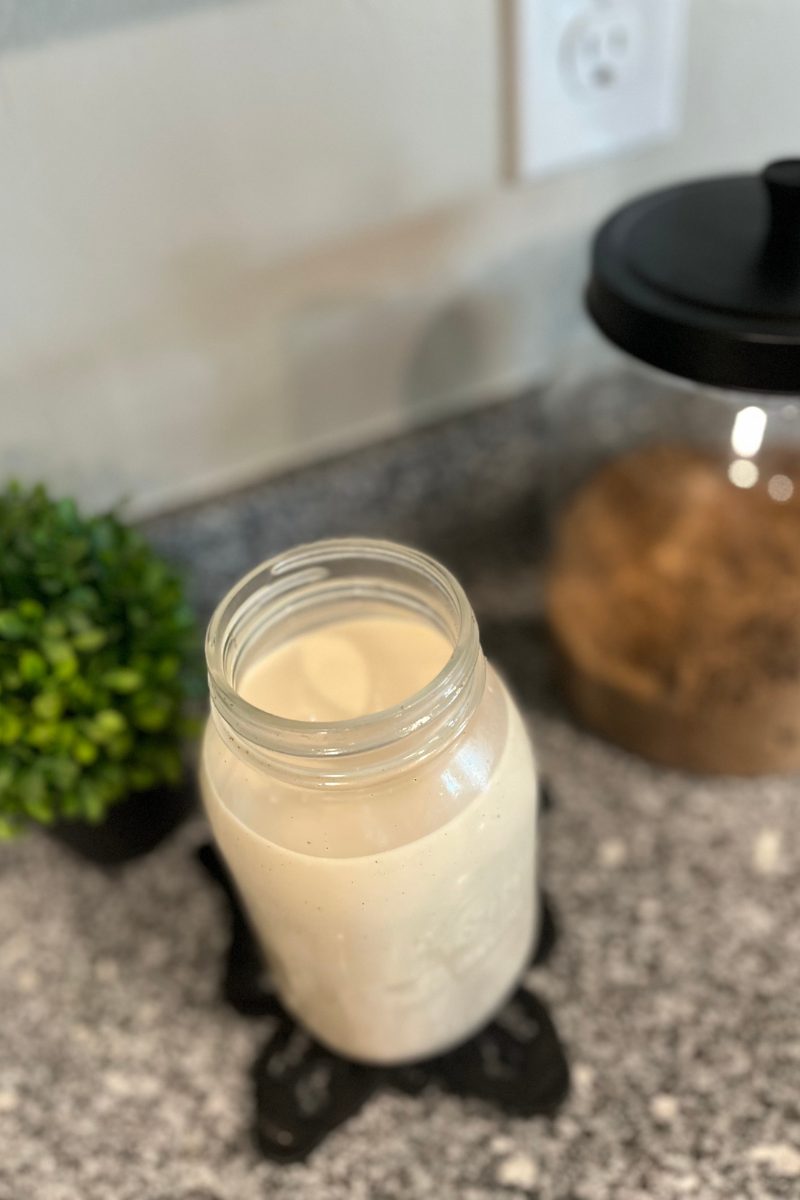 Cream in a glass mason jar with a green plant and jar of brown sugar behind